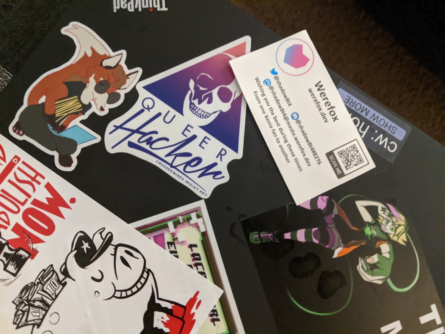 My thinkpad, decorated with stickers, including one of noted linux fox Xenia hunched over a laptop. Next to a Queer Hacker AOL logo sticker and a defund and abolish the police sticker.